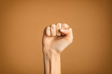 Hakları için savaşan el yazısı yapan bir kadın. El, kahverengi arka planda izole edilmiş parmakları yumruğa katlanmış. Kadın hakları, şiddete, eşitliğe ve bağımsızlığa karşı mücadele. 