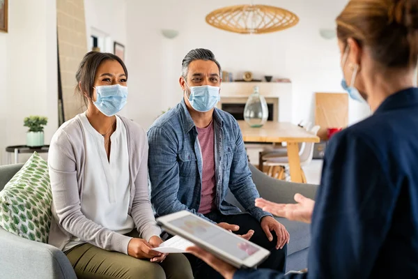 Young mixed race couple wearing face mask for precaution against covid-19 and discussing deal with agent. Happy indian man and beautiful black woman discussing real estate with agent wearing surgical mask for protection from covid. Businesswoman talk