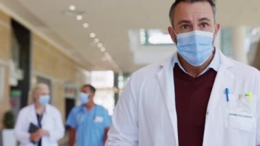 Klinikte yürüyen yorgun, olgun bir doktor. Kovid19 için laboratuvar önlüğü ve güvenlik maskesi takan pratisyen hekim hastanede yatan hastaları ziyaret ediyor. Yeni hastane pavyonunda çalışan endişeli doktor covid19 'dan dolayı..