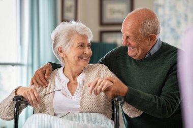 Romantik kıdemli koca engelli karısını kucaklıyor huzurevinde tekerlekli sandalyede oturuyor. Mutlu yaşlı çift kucaklaşıyorlar ve birbirlerine sevgiyle bakıyorlar. Çocuk yuvasında tekerlekli sandalyede oturan engelli kadının elini tutan mutlu yaşlı adam.. 