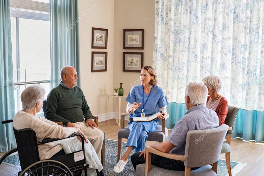 Group of senior people listening to young nurse. Psychological support group for elderly and lonely people in a community centre. Group therapy in session sitting in a circle in a nursing home facility