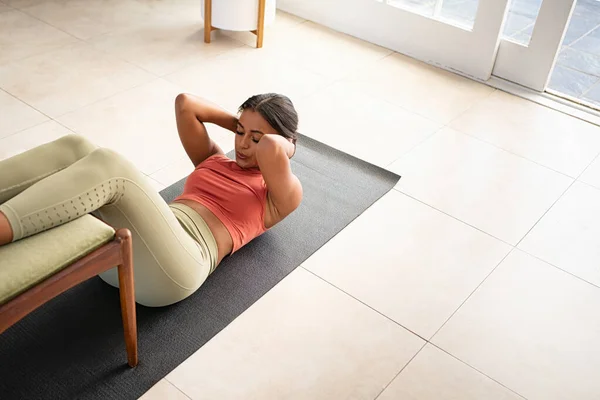 中年妇女躺在垫子上按压 同时把腿放在家里椅子上的头像 非洲裔美国妇女在早上的例行公事中在家练习嘎吱嘎吱声 健康的混血儿做腹肌运动并锻炼肌肉的高视角 — 图库照片