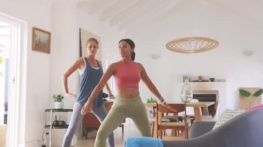 İki olgun kadın evde kollarını açmış savaşçı pozu veriyorlar. Sağlıklı olgun bir kadın oturma odasında melez bir ırk arkadaşıyla yoga yapıyor. Orta yaşlı kadın spor kıyafetleriyle evde birlikte egzersiz yapıyor..