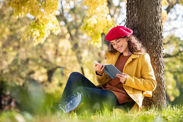 Parkta Düşen Sonbahar Yapraklarının Üzerinde Oturup Kitap Okuyan Güzel Genç — Stok fotoğraf