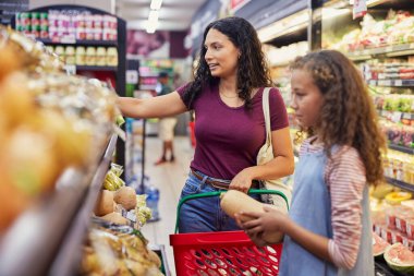 Genç, çok ırklı bir kadın, küçük kızıyla markette alışveriş yaparken taze sebze seçiyor. Çocuk markette annesini izlerken bir balkabağı tutuyor. Süpermarkette çok ırklı olmayan bir kadın taze meyve ve et alışverişi yapıyor.