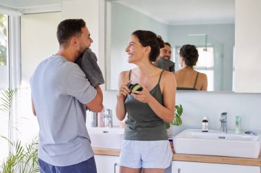 Erkek, kız arkadaşına bakarken lavabonun yanında tıraş olduktan sonra yüzünü havluyla kurutuyor. Güzel bir kadın gülümsüyor ve partneriyle konuşurken elinde bir kavanoz yüz kremi tutuyor. Yetişkin bir çift sabah vakti neşeli bir anı paylaşıyor.