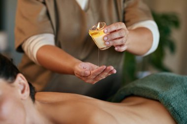 Kadın sırtına masaj yapmak için sıcak mum yağı döken masözün ellerine yaklaş. Spa terapisti yanan mumdan dönen kadına sıcak yağ döküyor. Kaplıca tedavisi sırasında yüzükoyun dinlenen kız.