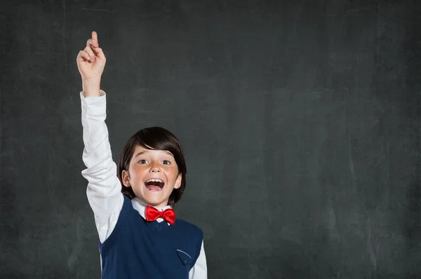 Little boy raising hand at blackboard Stock Picture