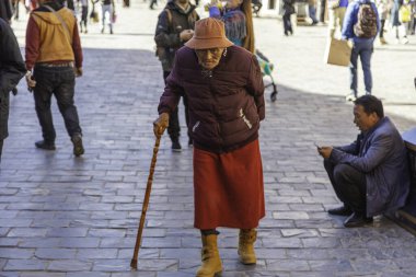 Lhasa, Tibet, Çin - 15 Kasım 2020: Jokhang Tapınak Meydanı 'nda koltuk değnekli eski Tibetliler. Geleneksel Tibet giysileri ve mavi şapkalı fakir görünümlü yaşlı adam.