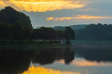Putra Meydanı etrafındaki parkın üzerinde güneş doğuyor Malezya hükümet şehri Putrajaya, Malezya 'da. Putrajaya Gölü 'nün üzerinde güzel bir gün doğumu ve tipik sabah sisi olan ağaçlar.