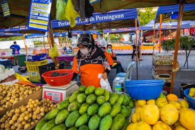 Başkent Kuala Lumpur yakınlarındaki Putrajaya 'da taze bir pazarda sebze tüccarları. Başörtüsü olan Müslüman kadın sebze satıyor. Covid-19 yüzünden yüz maskesi takıyor.