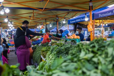 Başkent Kuala Lumpur yakınlarındaki Putrajaya 'da taze bir pazarda sebze tüccarları. Başörtüsü olan Müslüman kadın sebze satıyor. Covid-19 yüzünden yüz maskesi takıyor.