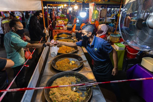 Kuala Lumpur yakınlarındaki Putrajaya 'daki sokak yemekleri pazarında. Müşteri aşçıya kızarmış eriştesinin parasını ödüyor. Yeni piyasada yüz maskesi zorunludur.