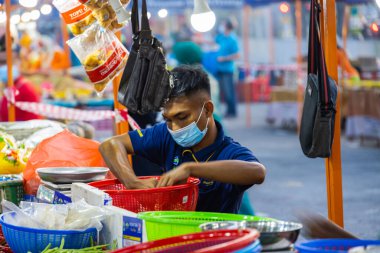 Başkent Kuala Lumpur yakınlarındaki Putrajaya 'da taze bir pazarda sebze tüccarları. Yüz maskeli genç adam sebzeleri tartıya koyuyor.