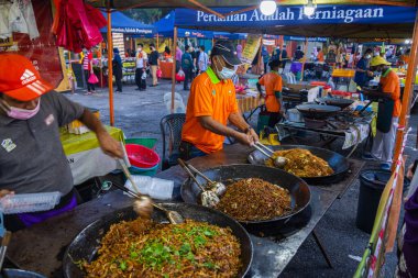 Kuala Lumpur 'da bir gece marketinde kızarmış erişte dükkanı. Tavadan geleneksel erişte satan iki namız var. Korona krizi yüzünden yüz maskesi takan adam....