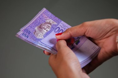 Kırmızı tırnaklı kadın eller 100 Ringgit banknotu sayıyor. Malezya 'nın para birimi Ringgit. Kadın elleri RM100 notaları gösteriyor. Malezya parasına renkli tırnaklarla yaklaş 