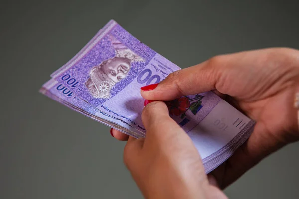Female Hands with red nails counting 100 Ringgit banknotes. Ringgit the currency of Malaysia. Woman hands showing RM100 notes. Close up to the Malaysian money with colorful fingernails