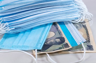 Yüz maskeleri, Japonya 'da yeni dünya para birimi 2020. Corona Cov19 krizi en çok aranan ekipman için yüz maskesi yapıyor. Fiyatlar yükseliyor. Beyaz arka planda Japon Yen parası olan ağız maskesi.. 