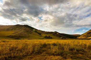 Güneş Moğolistan 'da batar, Arhangai-Aimag' daki Moğol bozkırında günbatımı manzara fotoğrafçılığı. Beyaz bulutlu mavi gökyüzü ve öndeki sarı bozkır otları
