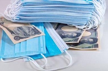 Yüz maskeleri, Japonya 'da yeni dünya para birimi 2020. Corona Cov19 krizi en çok aranan ekipman için yüz maskesi yapıyor. Fiyatlar yükseliyor. Beyaz arka planda Japon Yen parası olan ağız maskesi.. 
