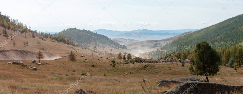 Panoramic view over the landscape of central Mongolia. The unsealed road to Ulaan Batar meanders through the landscape like a dusty rope or tape. The sand dust is visible on the horizon.