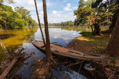 Siem Reap, Kamboçya yakınlarındaki küçük bir gölde geleneksel uzun kuyruklu ahşap tekne. Gökyüzü ve etrafındaki ağaçlar suya yansıyor. Kamboçya 'nın en çok ziyaret edilen yerinin hemen yanında.