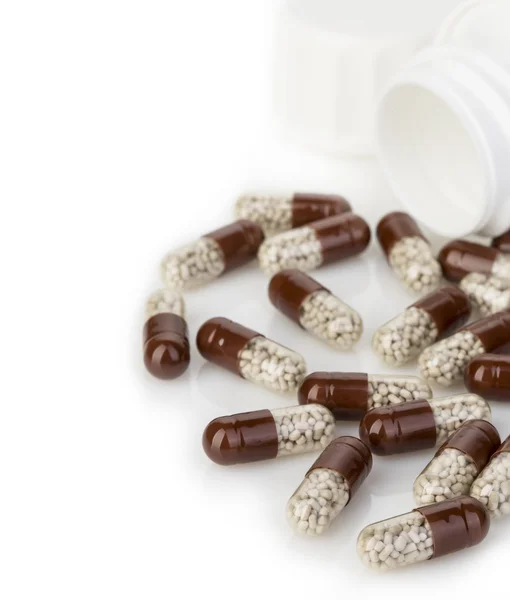 Brown capsules, pills poured out of a white bottle close-up on a white background. — Stock Photo, Image