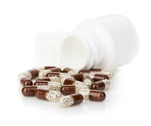 Brown capsules, pills poured out of a white bottle close-up on a white background. — Stock Photo, Image