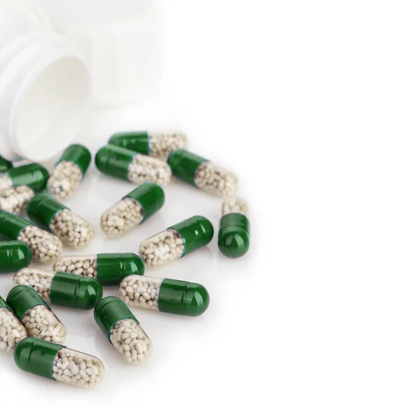 Cápsulas verdes, pastillas vertidas de un frasco blanco de cerca sobre un fondo blanco . Fotos de stock