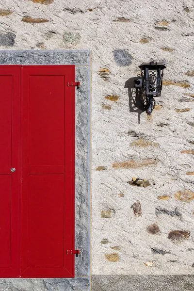 Closed red door and light on the stone wall - a geometric display