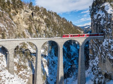 Filisur İsviçre - 31 Ocak. 2019: Meşhur Landwasser Viaduct 'u geçen kırmızı bir İsviçre treni - insansız hava aracı tarafından aeiral bir görüntü