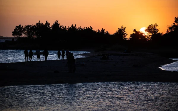 A group of people silhouetted against the sunset on Sandy Hook in New Jersey.
