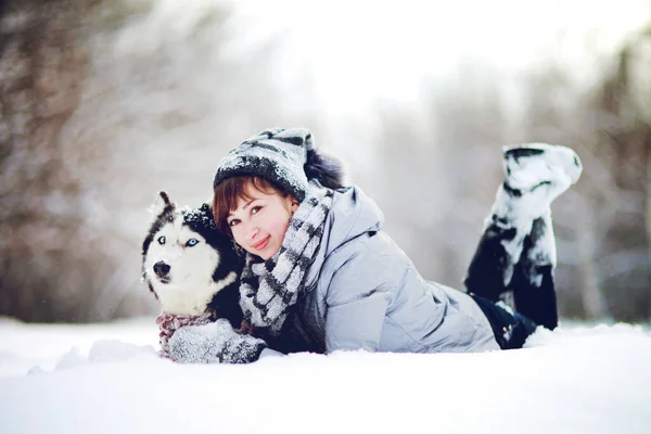 Дівчина лежить на снігу з сибірським хаскі собакою в зимовому лісі — стокове фото