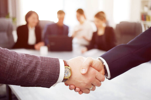 Business people shaking hands finishing a meeting in the background of their work team. 