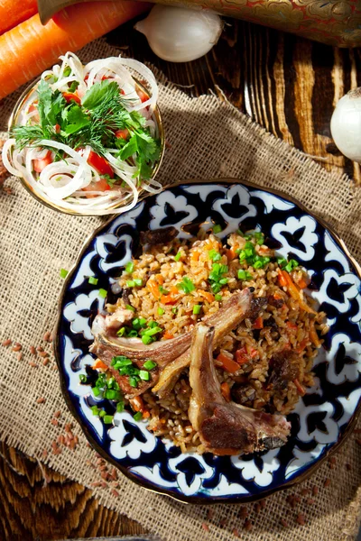 Pilaff - ris med lammkotletter och grönsaker. Garnerad med lök och tomater sallad — Stockfoto