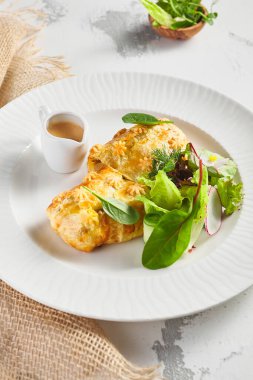 Karaciğer ve krema soslu turta. Taze yeşil yapraklarla süslenmiş. Çuval bezli beyaz tabak.