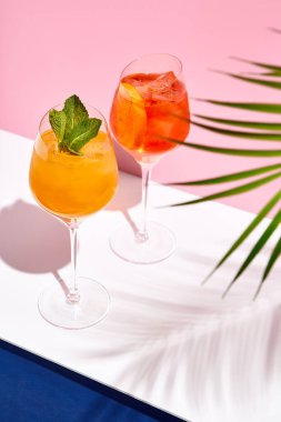 Beyaz masaya Spritz kokteyli. Tropik palmiye yaprağı gölgesi. Yaz kokteyl grubu. Pembe ve klasik mavi arkaplan