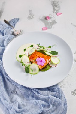 Kabaklı somon filetosu ve brokoli köpüğü (espuma). Çiçekler ve taze yeşilliklerle süslenmiş.