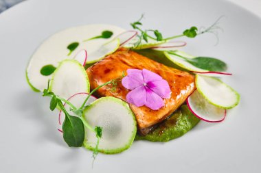 Kabaklı somon filetosu ve brokoli köpüğü (espuma). Çiçekler ve taze yeşilliklerle süslenmiş.