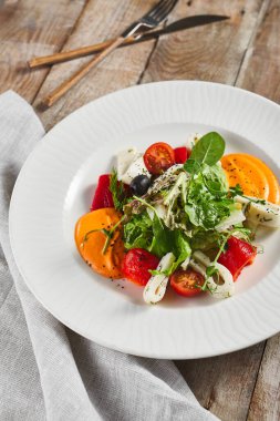 Kalamar ve taze yeşillikle kavrulmuş biber salatası. Kırsal ahşap masa ve gri tekstil