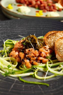 Salatalıklı somon tartar ve ekmek tostu. Siyah restoran tabağı.