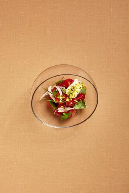 Yuvarlak cam kasede stracciatella ile domatesler. Domates salatası manzaralı. Lüks restoran garnitürü. Şeftali arkaplanlı gurme yemeği kursu. Yemek sunumu sanatı. Güzel yemek.