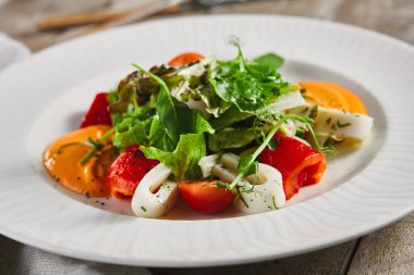 Kalamar ve taze yeşillikle kavrulmuş biber salatası. Kırsal ahşap masa ve gri tekstil