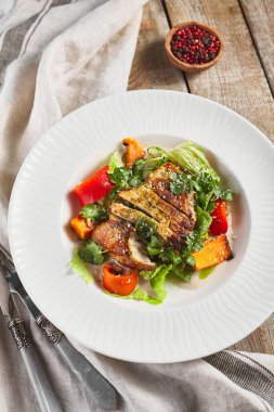 Fırında sebze salatalı tavuk fileto. Tahta masa ve gri peçete. Beyaz plakalı köylü tarzı.