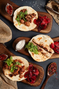 Düz ekmekli garnitürlü kebap. Tahta tabakla süslenmiş. Siyah sayfa arkaplanı