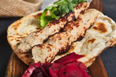 Düz ekmekli garnitürlü kebap. Tahta tabakla süslenmiş. Siyah sayfa arkaplanı