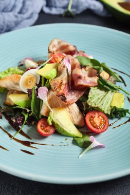 Avokadolu salata, hindi eti ve pastırma. Koyu dokulu masada mavi tabak. Restoran, keto diyet danışmanı.