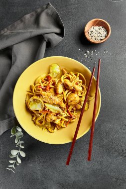 Körili Udon Eriştesi. Sarı tabakta Asya körili udon. Koyu tahtada ahşap yemek çubuğu. Asyalı, otantik gıda konsepti.