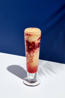 Beyaz ve mavi arka planda ahududu ve muzlu smoothie. Gün ışığı ve sert gölgeli palmiye yaprağı. Meyveli yoğurt ya da buzlu bardakta sallanan içecek. Yaz, sağlıklı, taze içecek konsepti