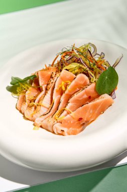 Susamlı somon balığı ve salata. Balık sashimi restoran aperatifi yeşil duvarlı beyaz masada. Tropik palmiye yapraklarının sert gölgesiyle gün ışığı. Yaz ya da bahar yemekleri
